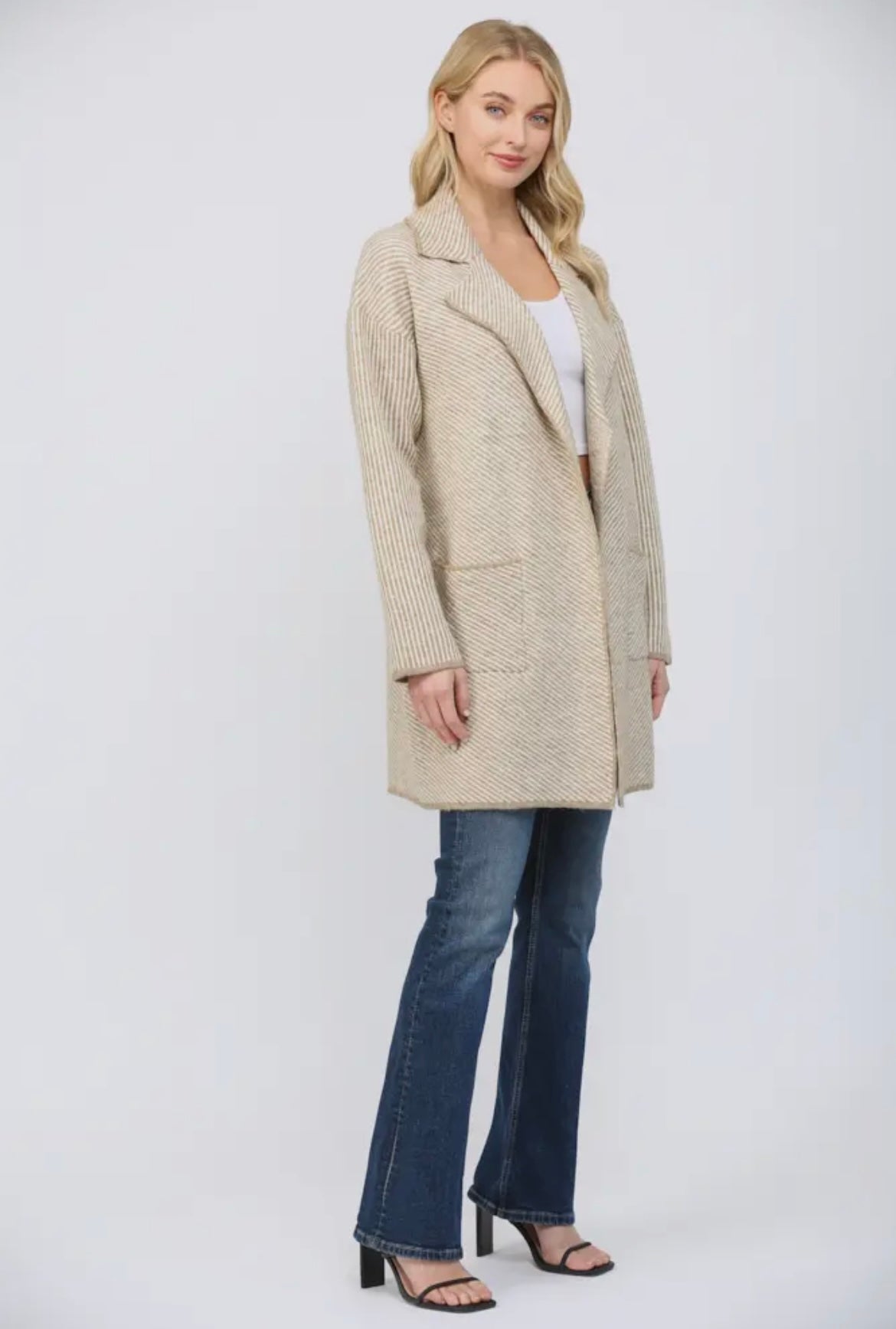 Woman wearing a beige coat and blue jeans on a white background