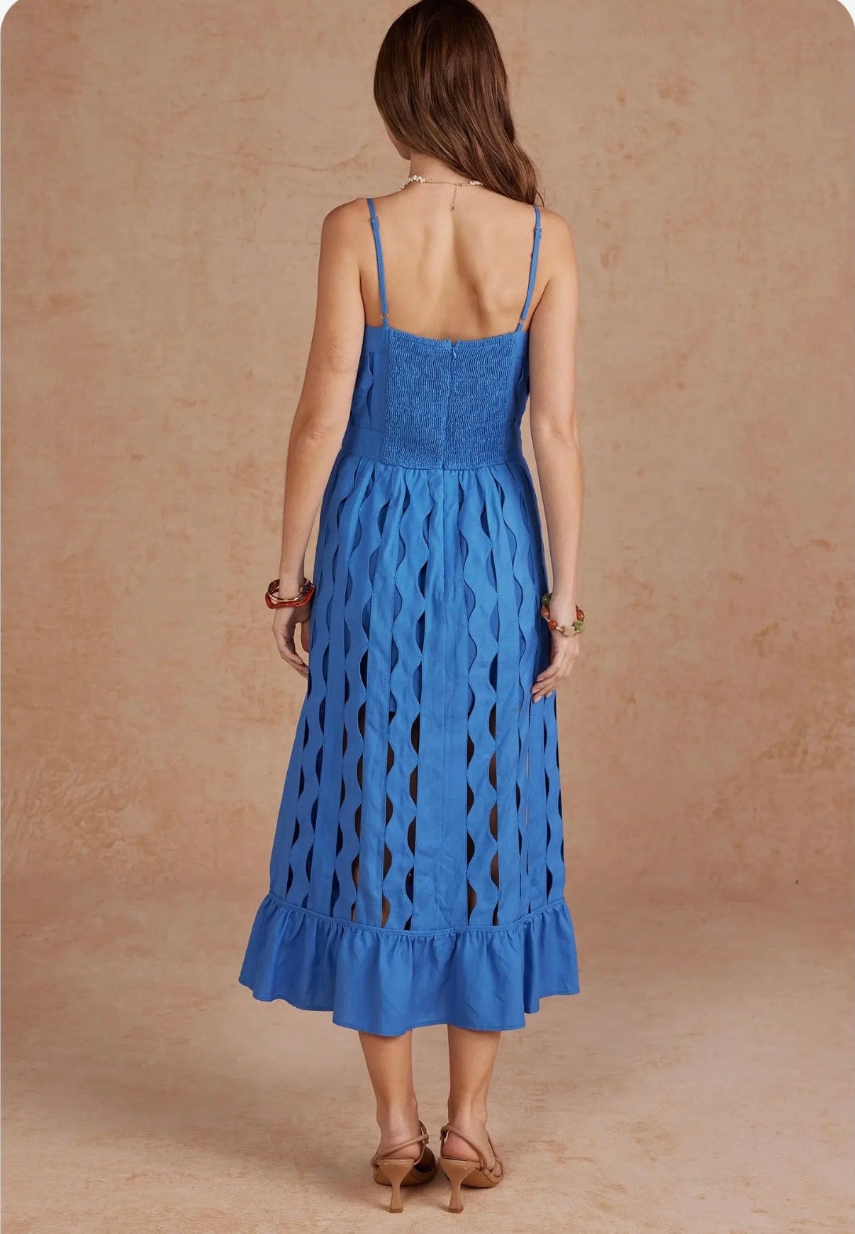 Woman wearing a blue dress with cut-out patterns on a beige background