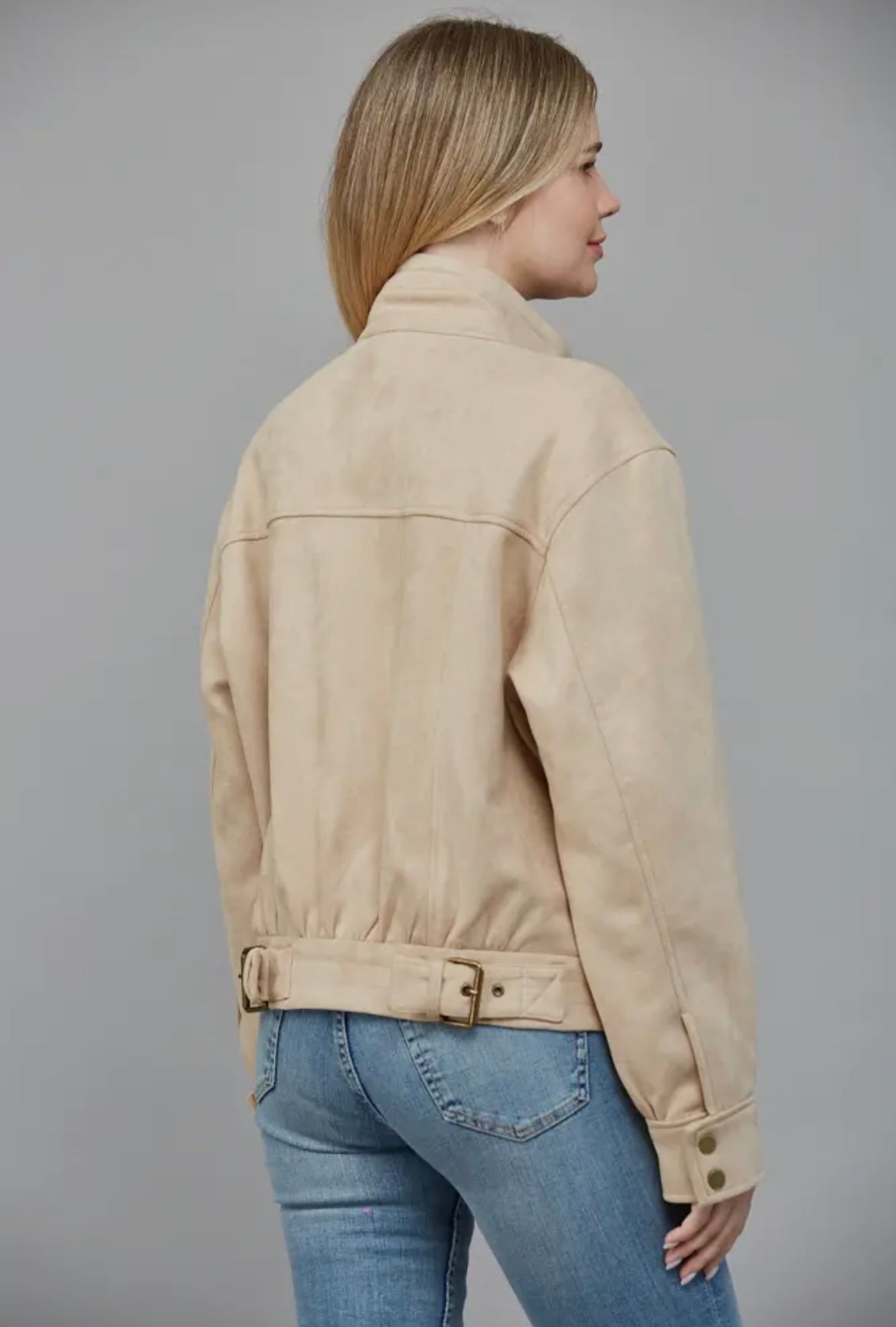 Woman wearing a beige jacket and blue jeans against a gray background