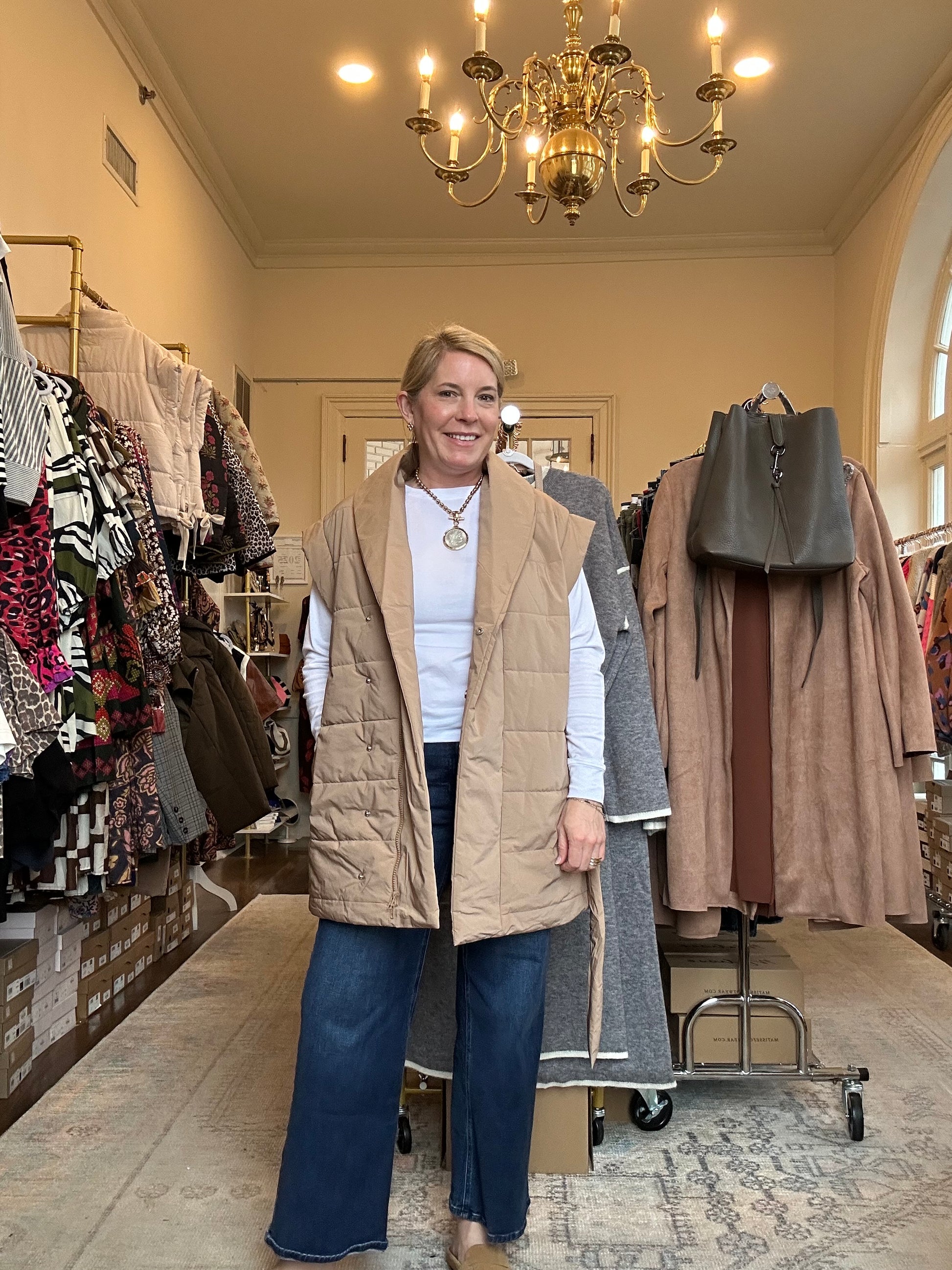 Person standing in a store with clothes on racks and a chandelier in the background