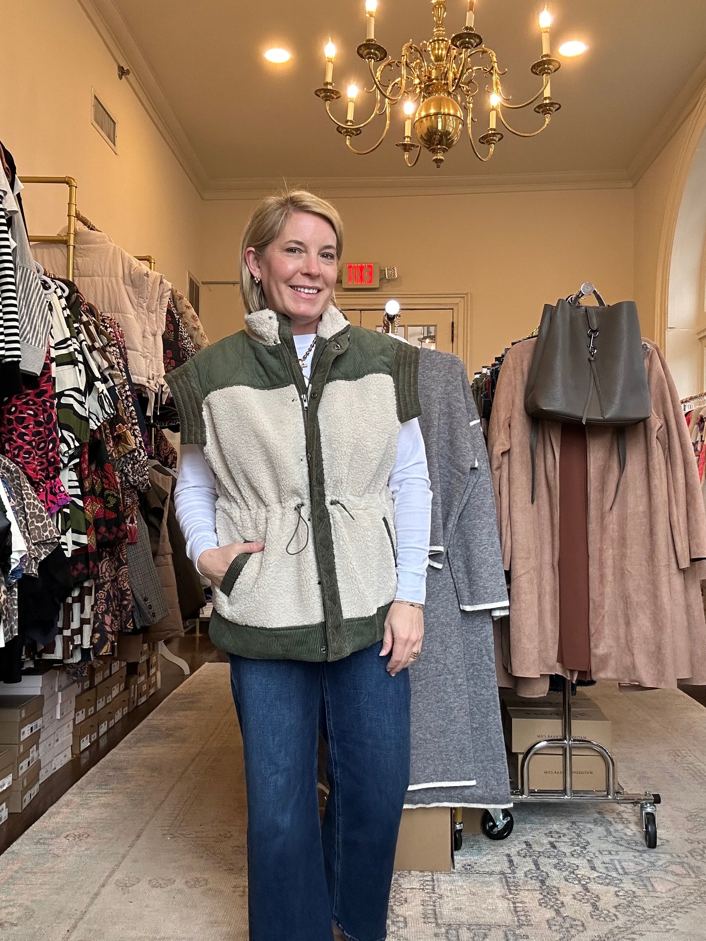 Woman in a clothing store trying on a gray vest.