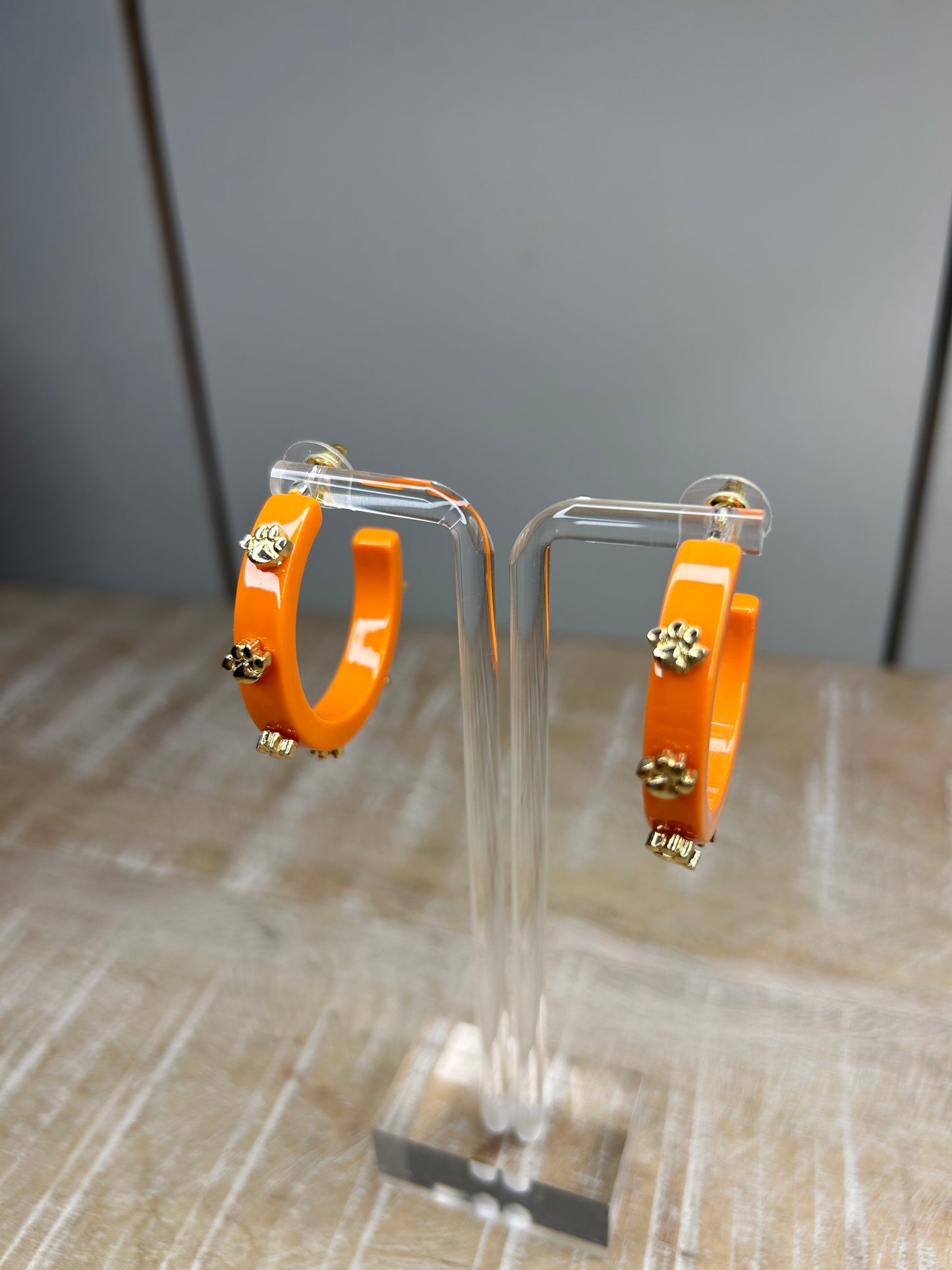 Orange hoop earrings with gold 3D paws evenly placed on the hoops