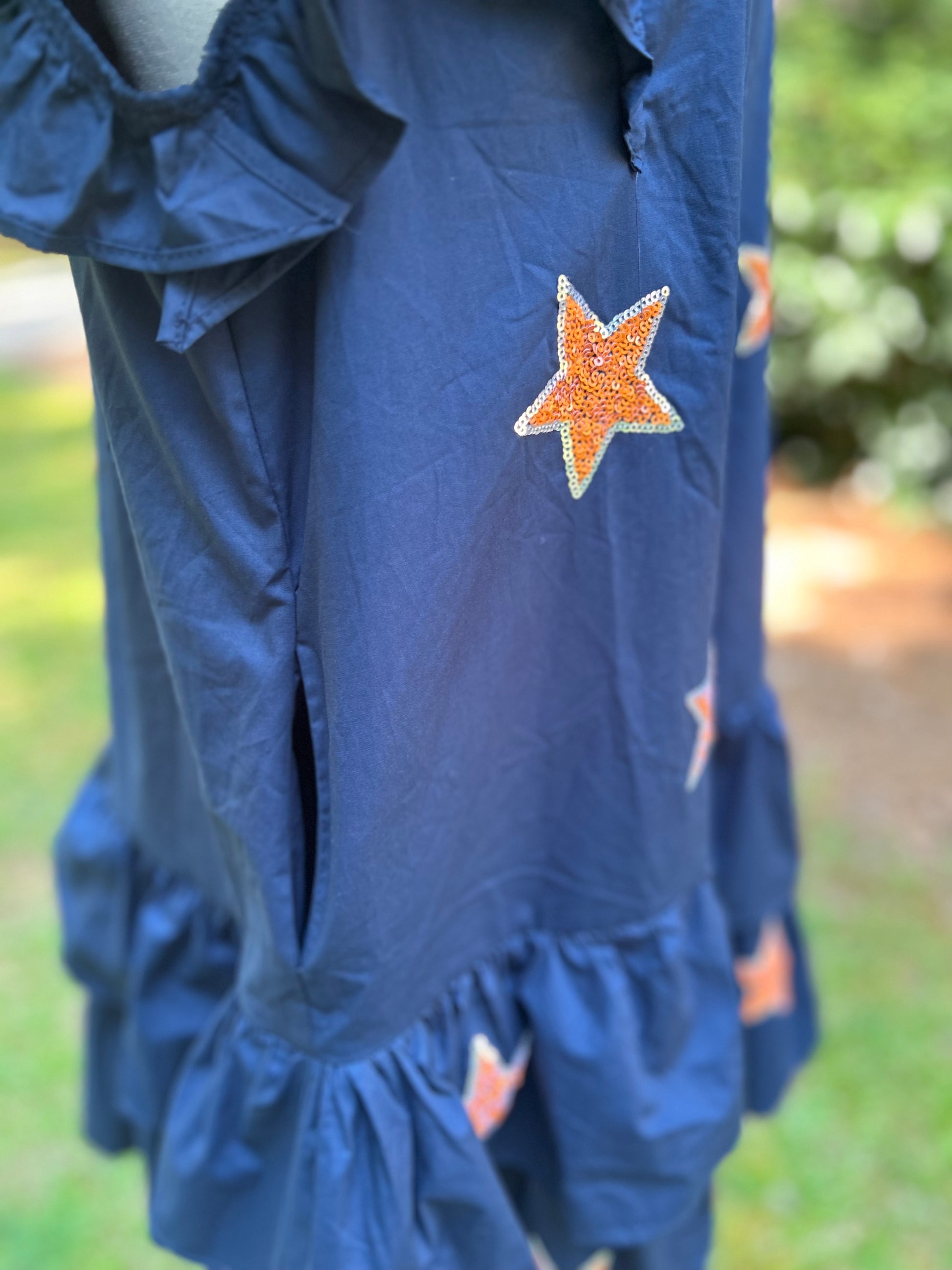 Sequin stars in orange on the front of a navy ruffled dress.
