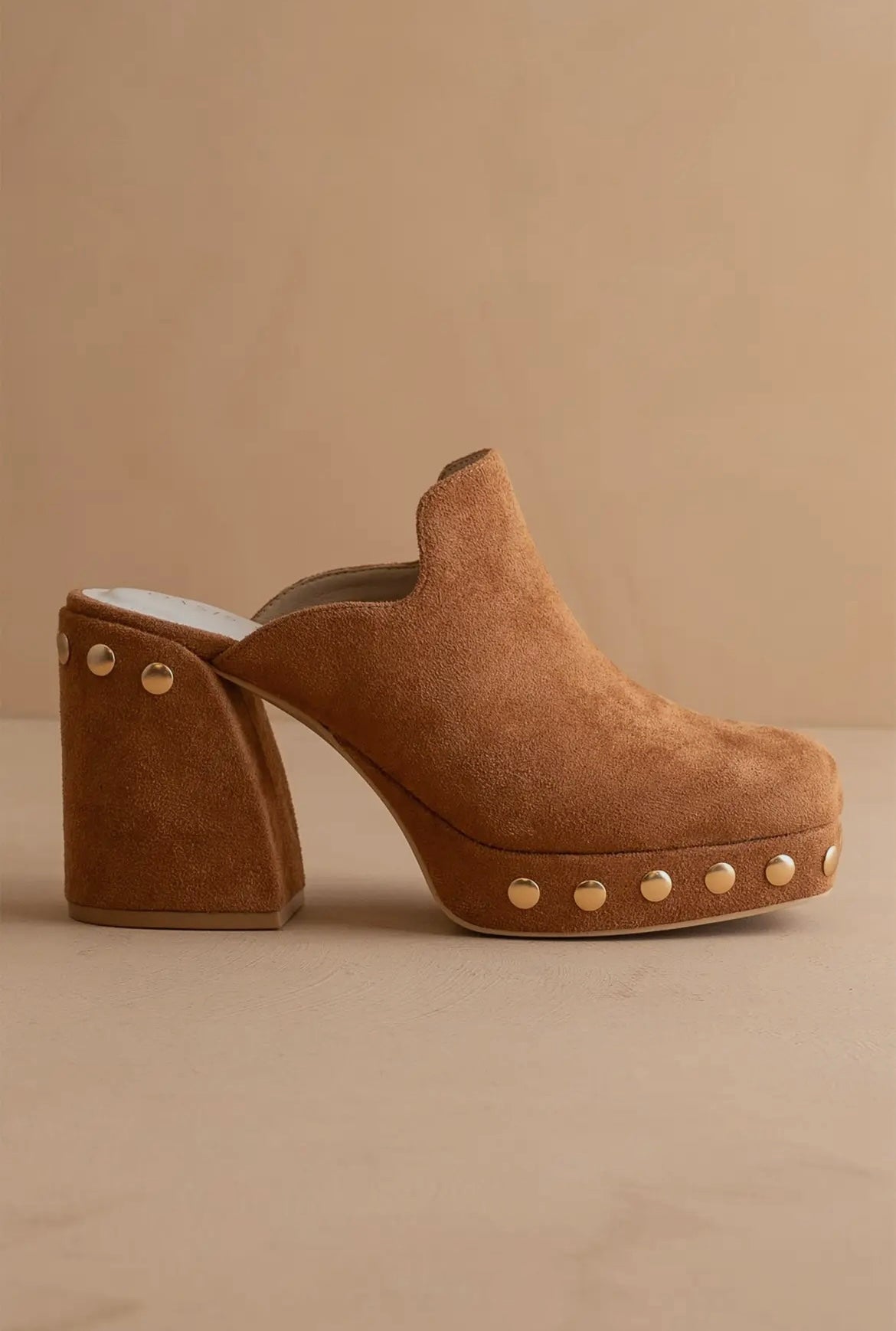 Brown suede clog shoe with gold studs on a beige background