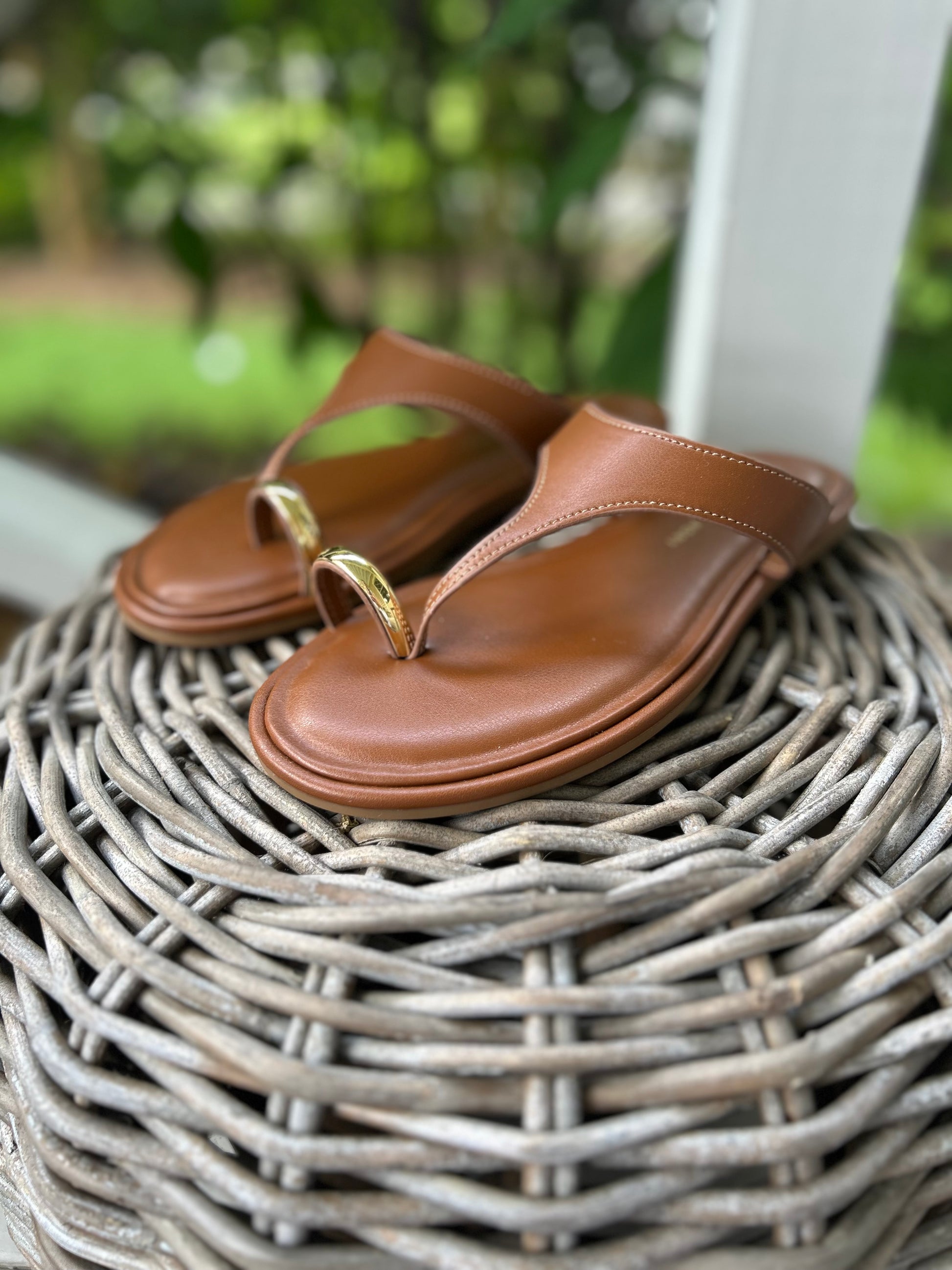 Flat tan sandals with a gold toe-strap